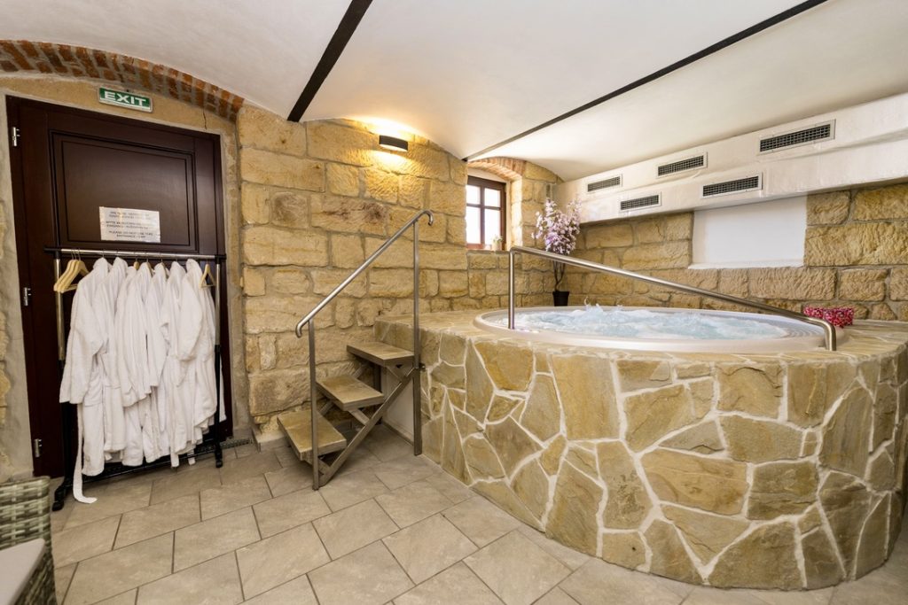 Round hot tub with natural stone surround, access steps, stainless steel handrail and white bathrobes at Resort Mezná.